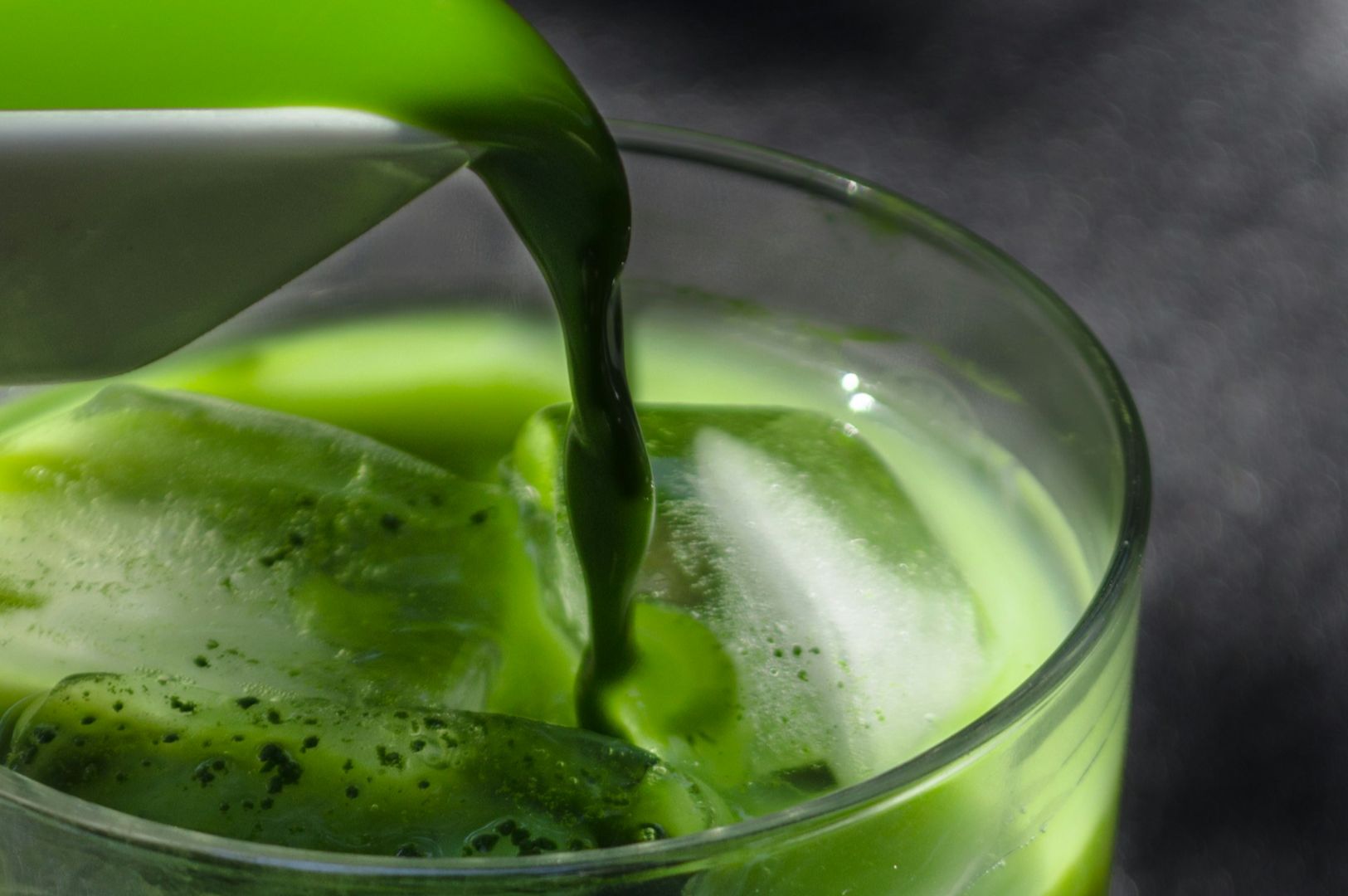 Close-up of vibrant green matcha tea being poured into a glass with ice cubes, creating a refreshing and invigorating visual contrast.