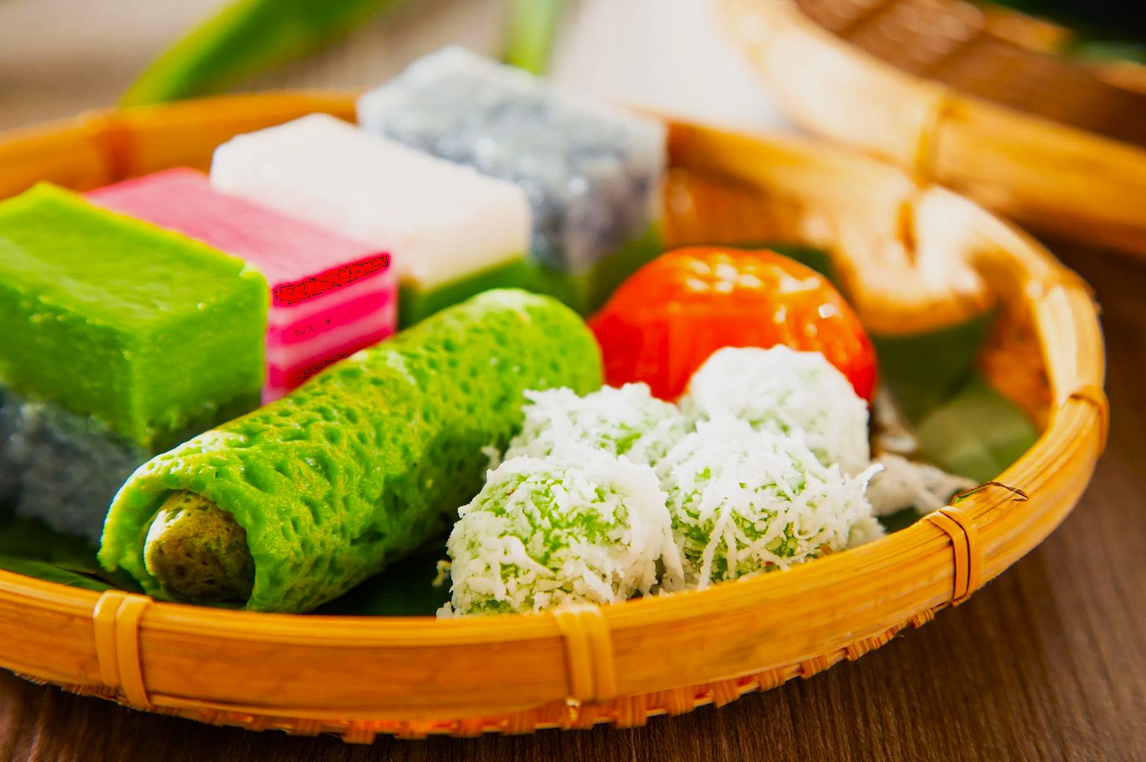A basket of Malaysian kuih, showcasing colorful coconut-coated balls, a green rolled crepe, and vibrant layered cakes, evoking a sense of delight.