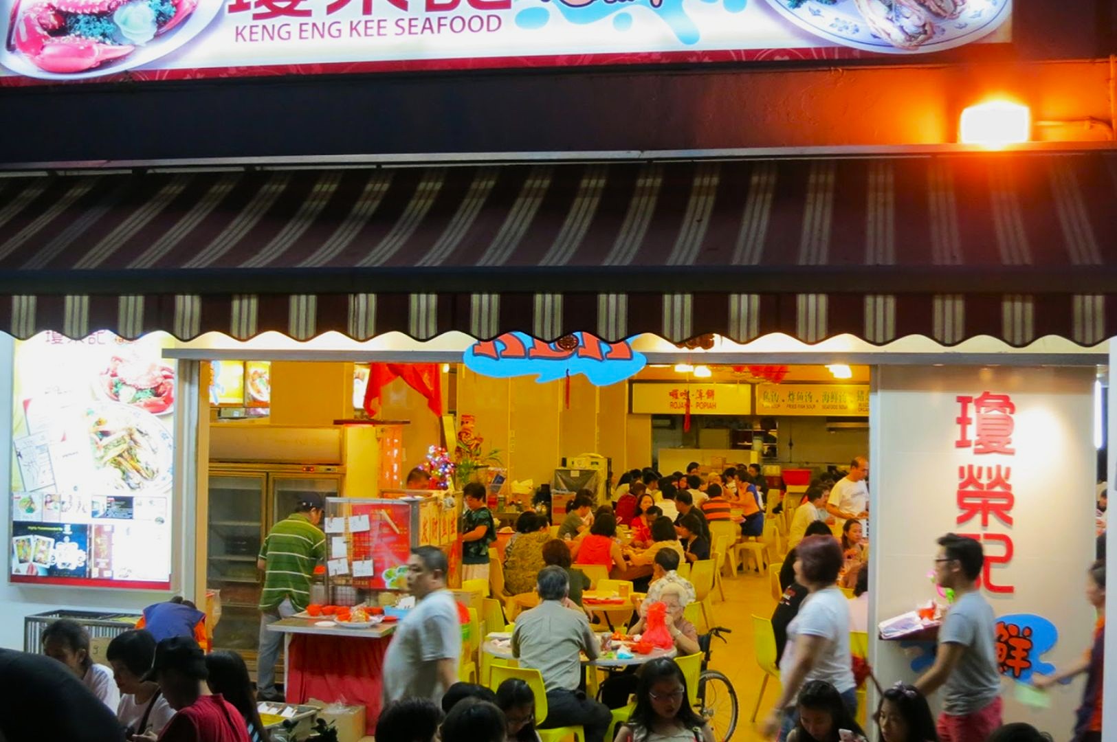 A bustling seafood restaurant at night, full of diners at yellow tables, conveys vibrancy and liveliness. Red signage and decor give a festive, welcoming feel.