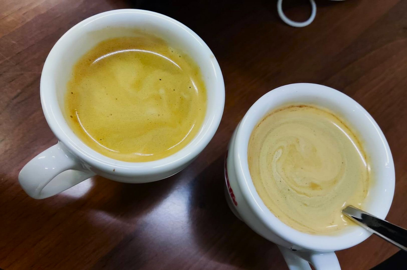 Two white mugs of golden espresso on a wooden table, showcasing creamy swirls on the surface. A relaxed and inviting coffee break setting.