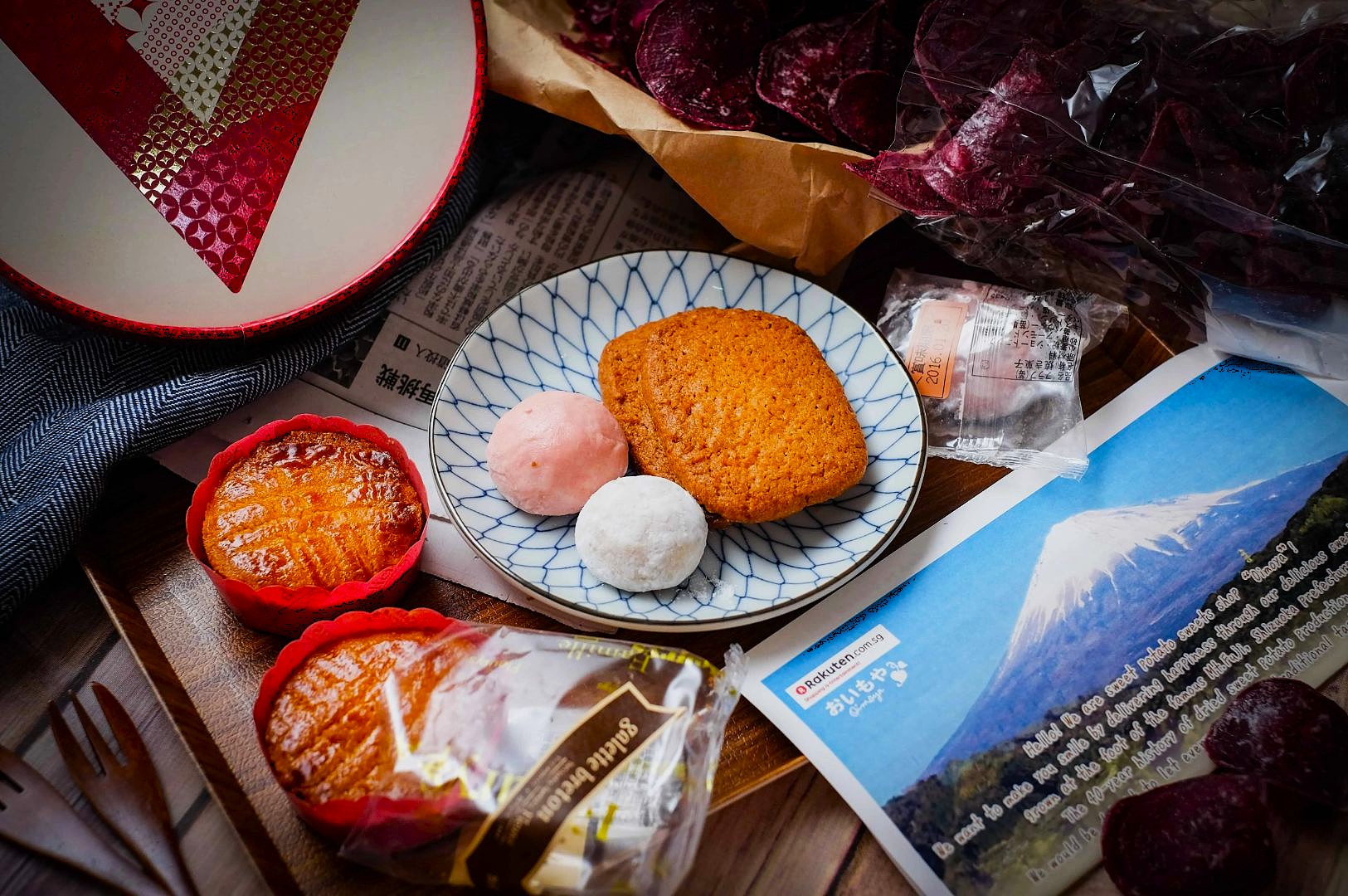 A variety of Japanese snacks are artfully arranged. A plate with cookies, pink and white mochi is the centerpiece. A photo of Mount Fuji and other snacks surround it, creating a cozy, inviting atmosphere.