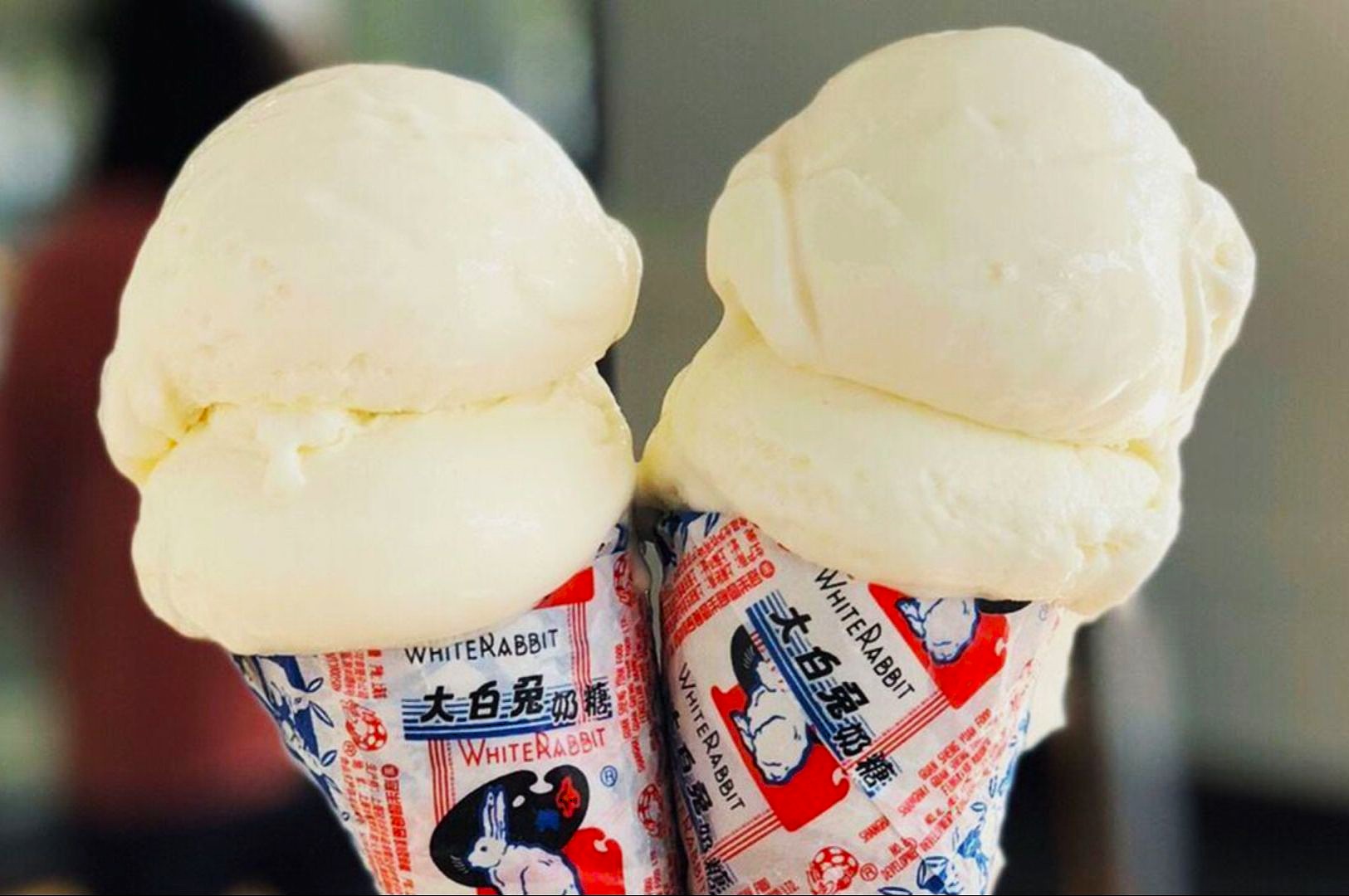 Two scoops of creamy vanilla ice cream rest on cones wrapped in colorful White Rabbit candy packaging, evoking a nostalgic and playful mood.