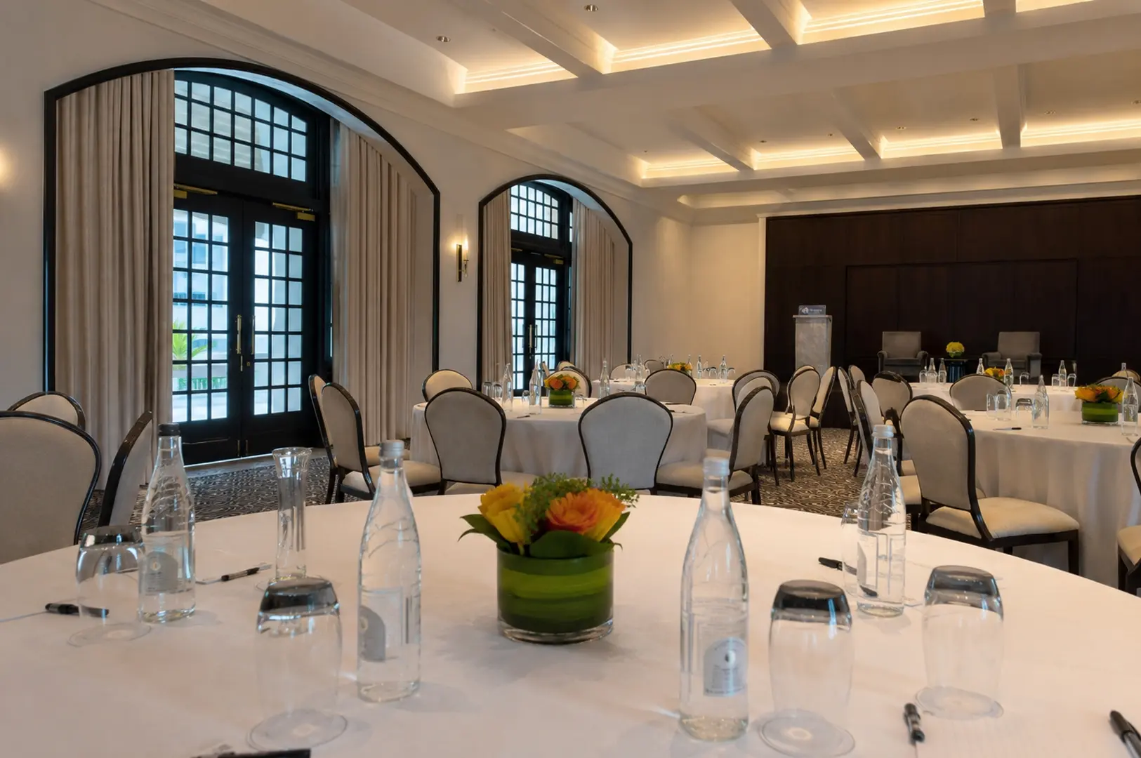 Spacious private dining room with round tables, white linens, and large arched windows