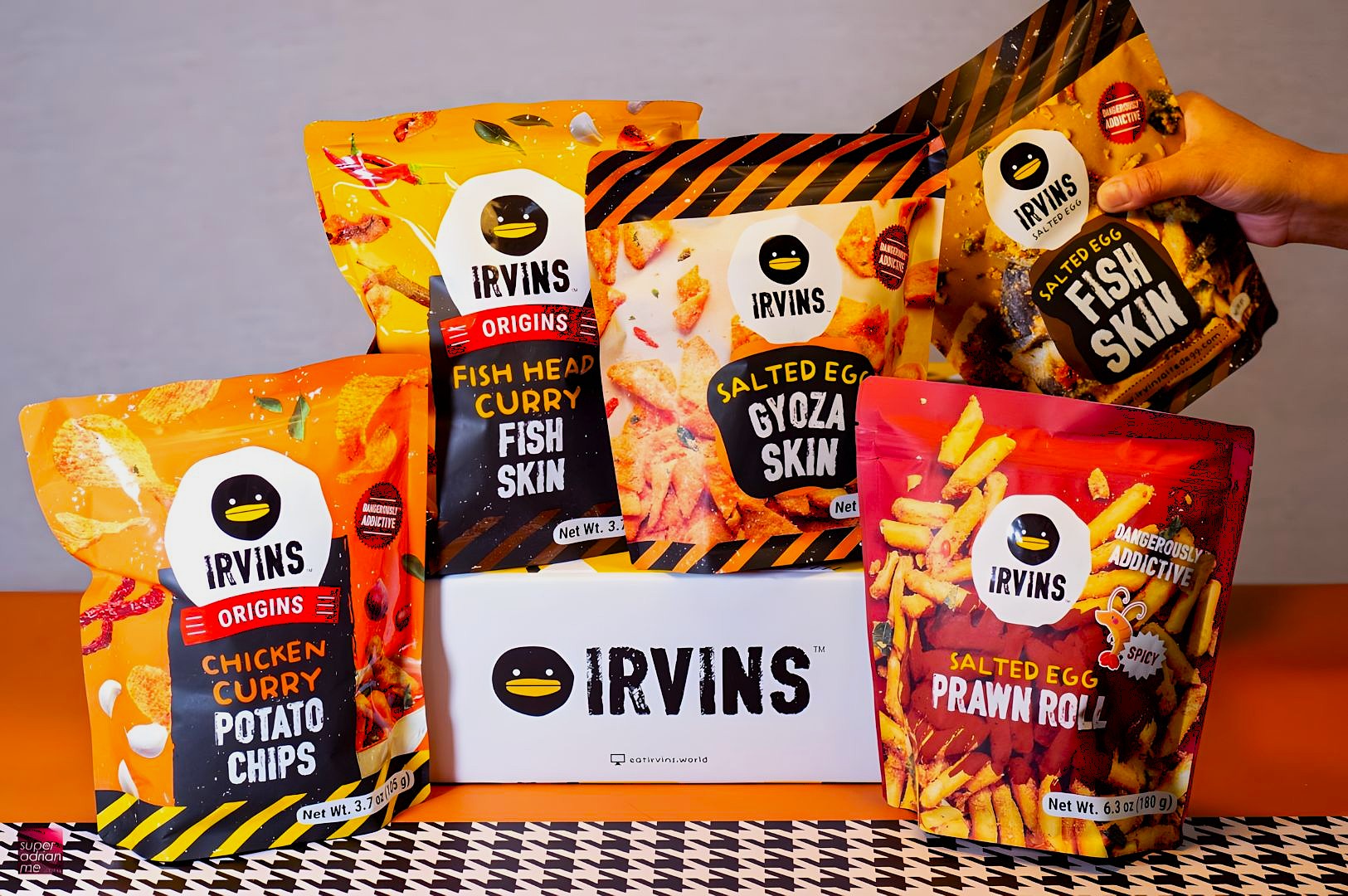 A colorful display of IRVINS snack bags—fish skin, gyoza skin, chicken curry potato chips, and prawn roll—arranged around a white IRVINS box, highlighting salted egg snack flavors and bold packaging.