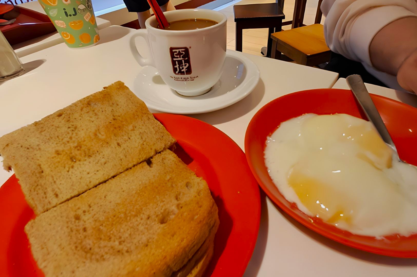 Toasted bread and soft-boiled eggs on red plates sit on a white table alongside a cup of coffee in a white mug, creating a cozy breakfast scene.