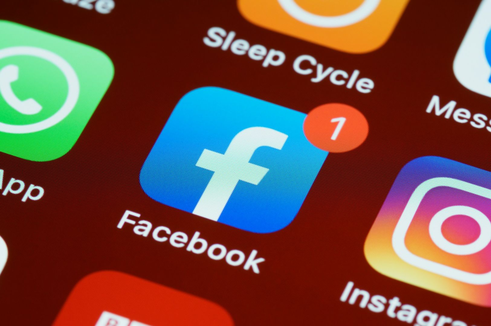 Close-up of a smartphone screen showing app icons, including Facebook with a notification badge, Instagram, WhatsApp, and Sleep Cycle on a red background.