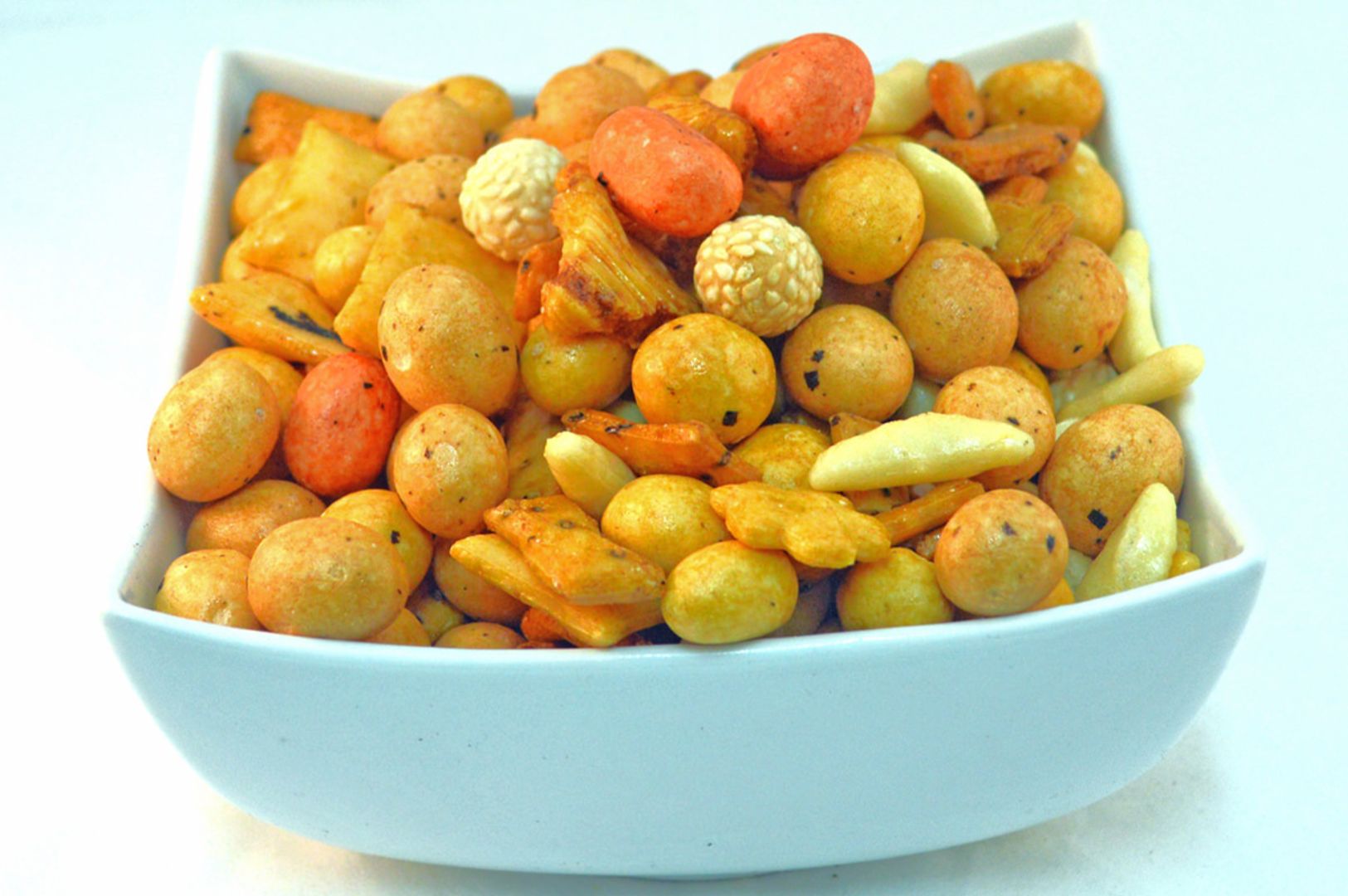 A white bowl filled with a variety of crunchy nut snacks, including spiced lentil balls, sesame-coated treats, and vibrant fried snacks. The mix appears savory and appetizing.