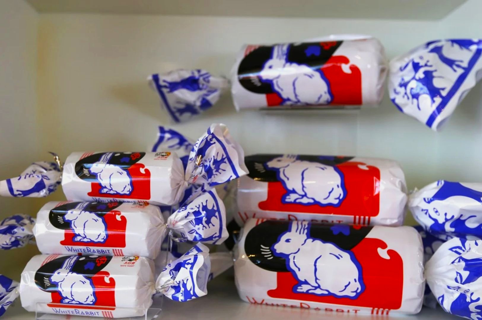 Packages of White Rabbit candy are arranged on shelves. The wrappers feature a blue and red rabbit design, creating a nostalgic and playful feel.