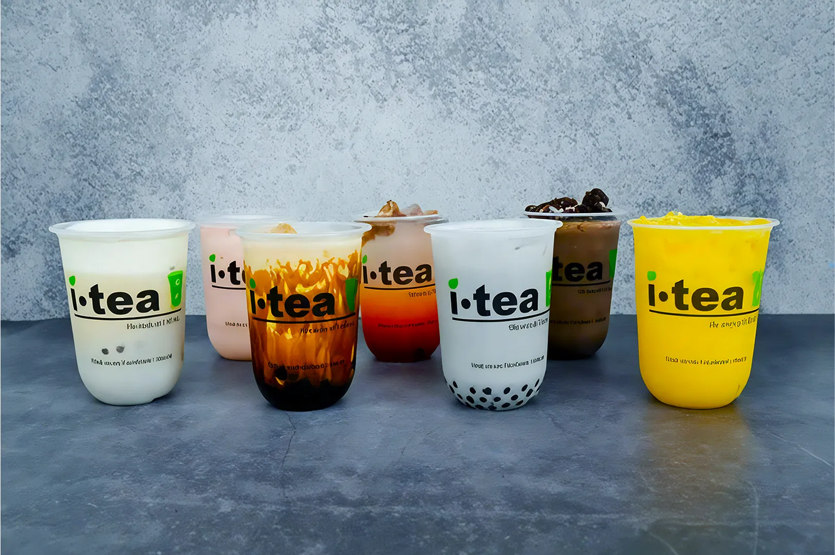 A lineup of six colorful bubble tea cups on a gray surface with a textured wall. Each has a unique flavor, creating a vibrant and inviting display.
