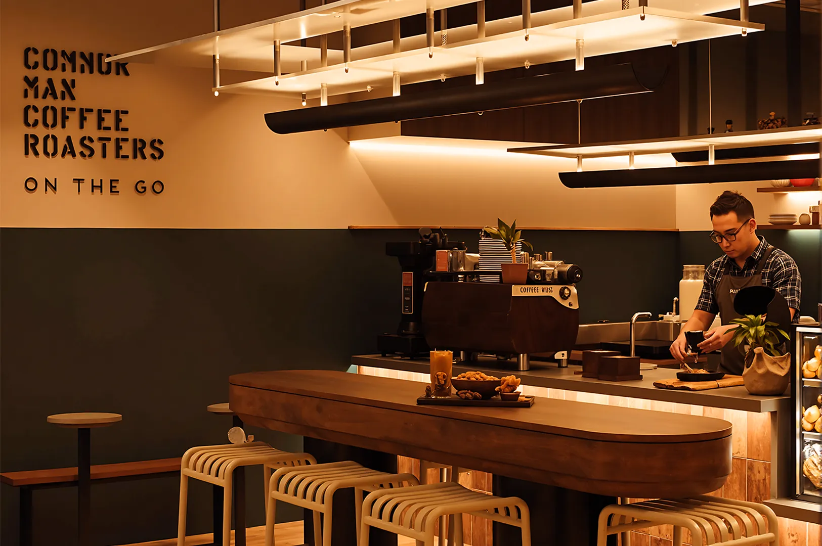 Cozy coffee shop with a modern design, featuring a barista preparing coffee. Warm lighting, wooden tables, and stools create a welcoming atmosphere.