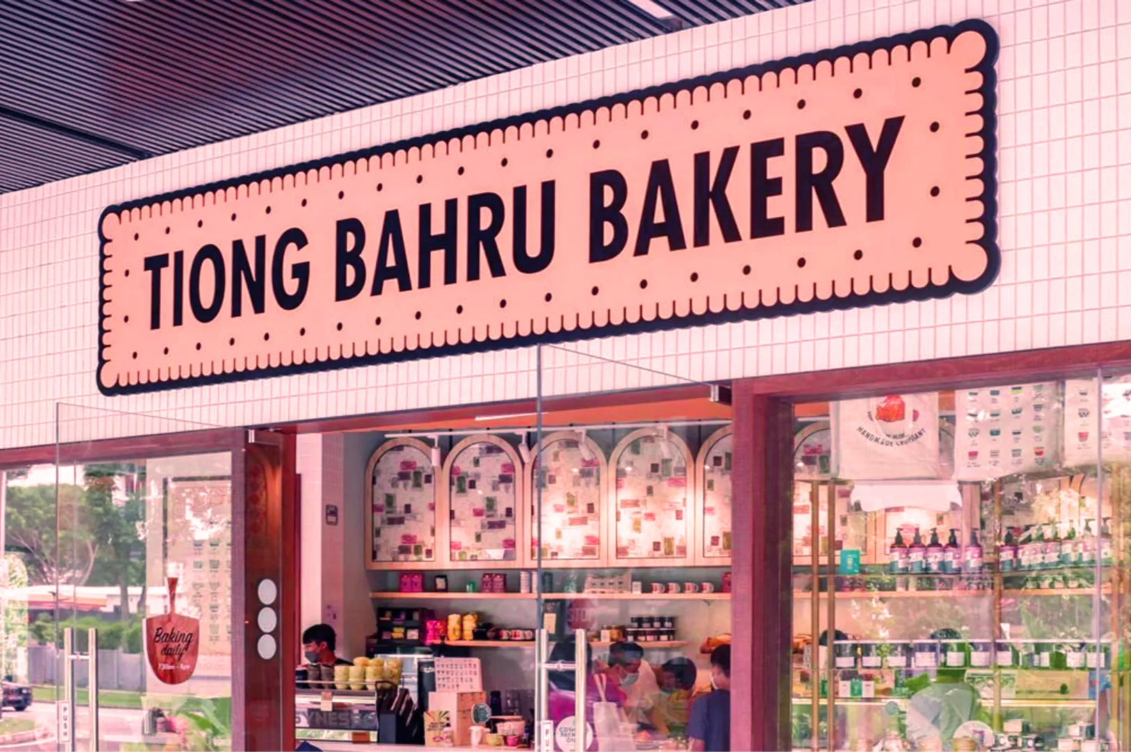Exterior of Tiong Bahru Bakery with a large, bold sign. The interior is visible, showcasing colorful products and a warm, inviting atmosphere.