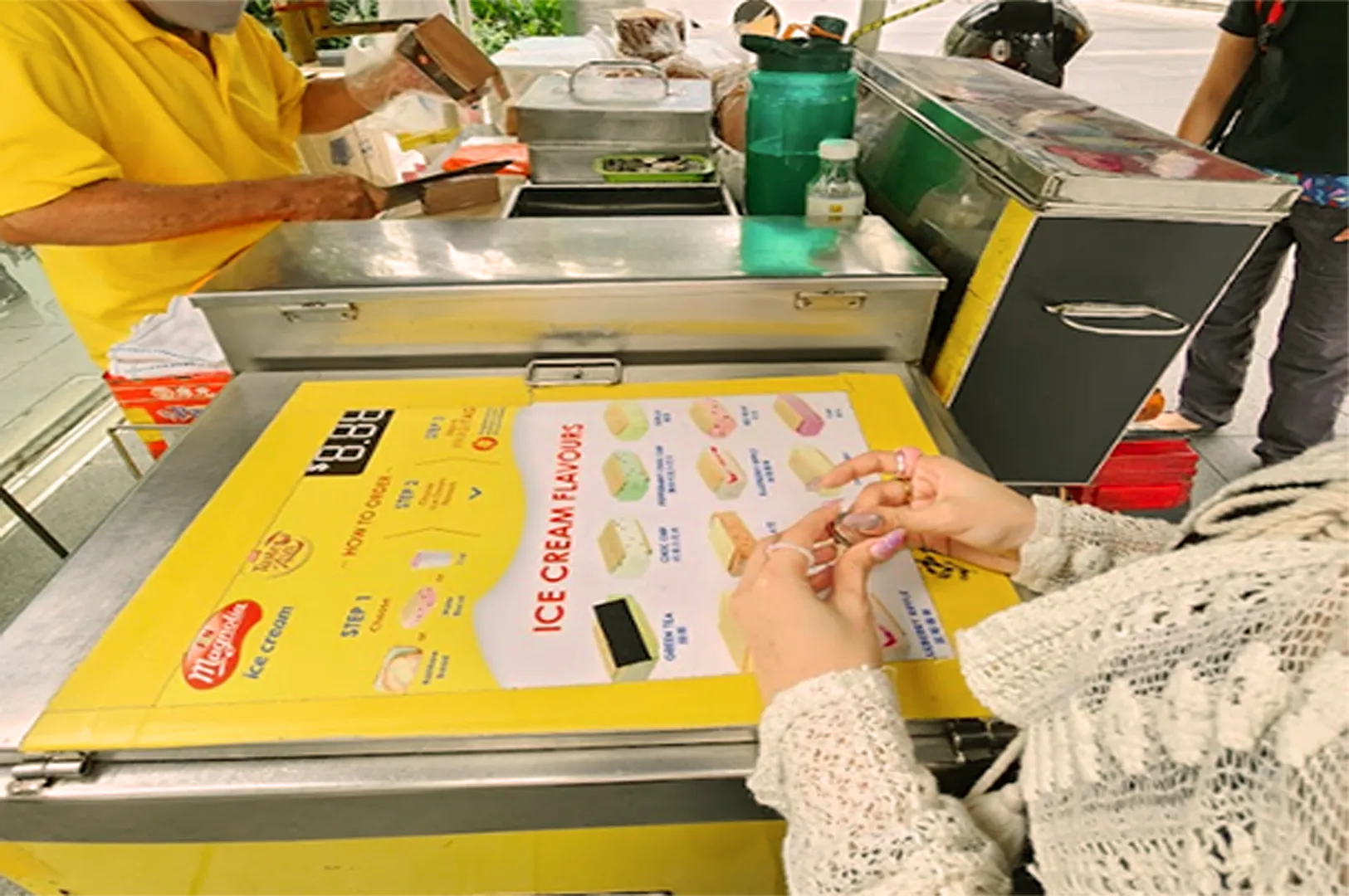 A street vendor in a yellow shirt prepares ice cream.
