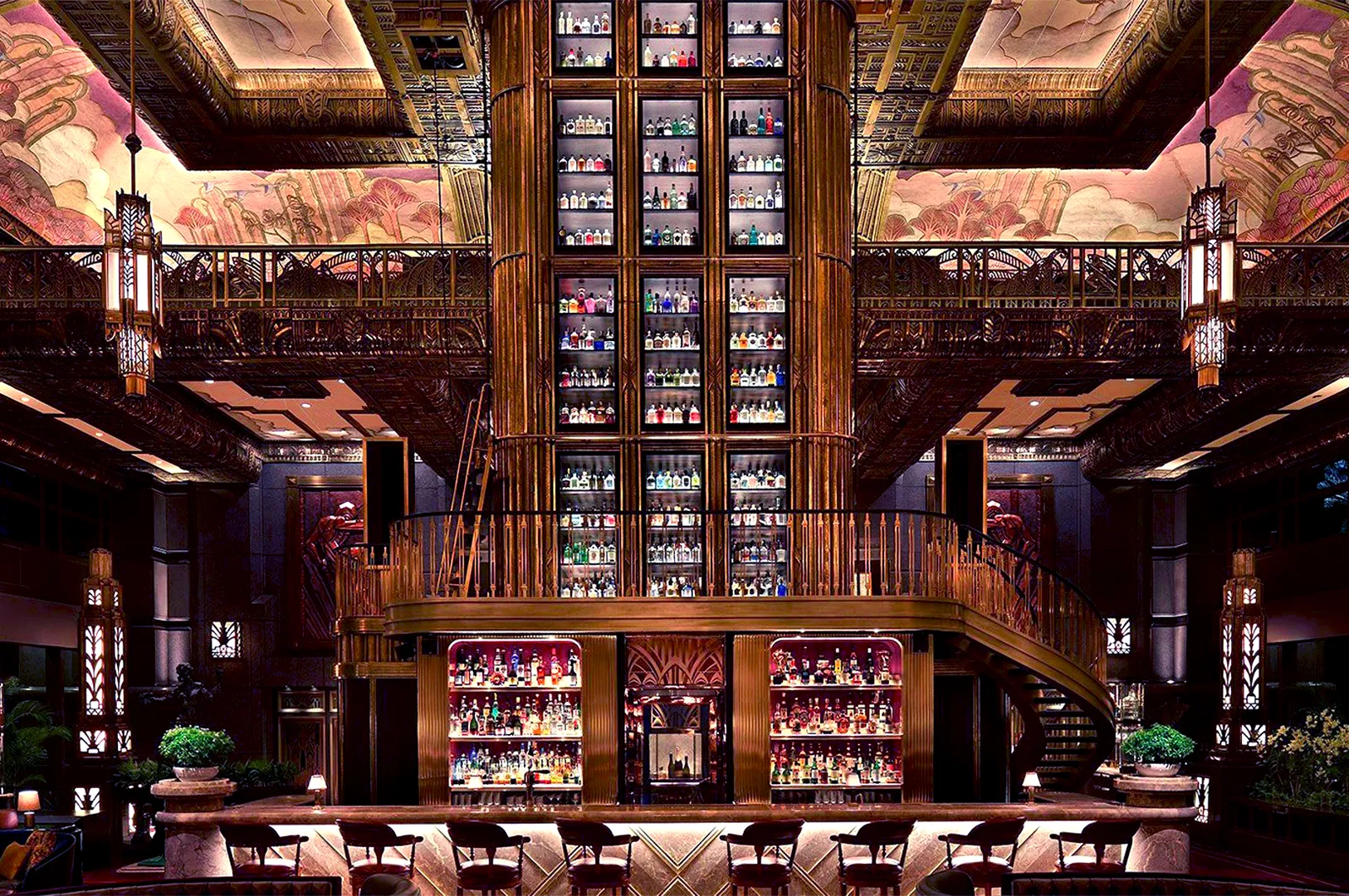 Lavish bar with a towering, illuminated liquor shelf and spiral staircase. Art Deco design, ornate ceiling, warm lighting, opulent, elegant atmosphere.