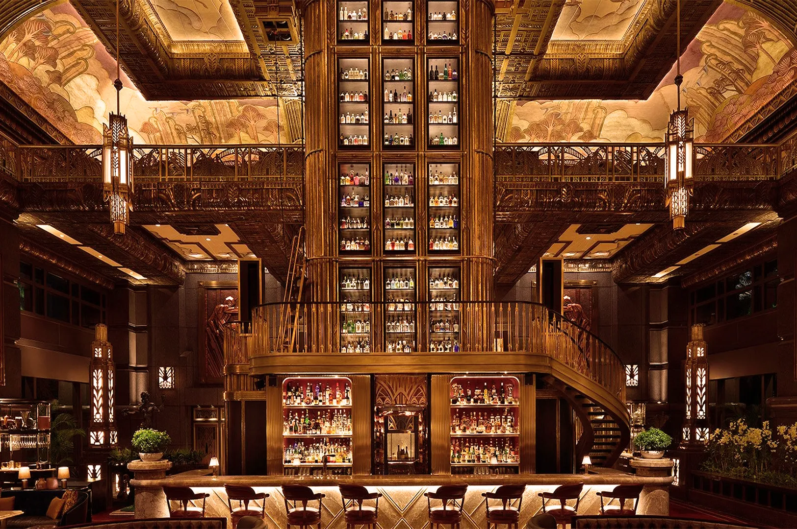 Opulent bar with grandiose ceiling, intricate murals, and a towering central liquor display. Warm lighting and plush seating create a luxurious atmosphere