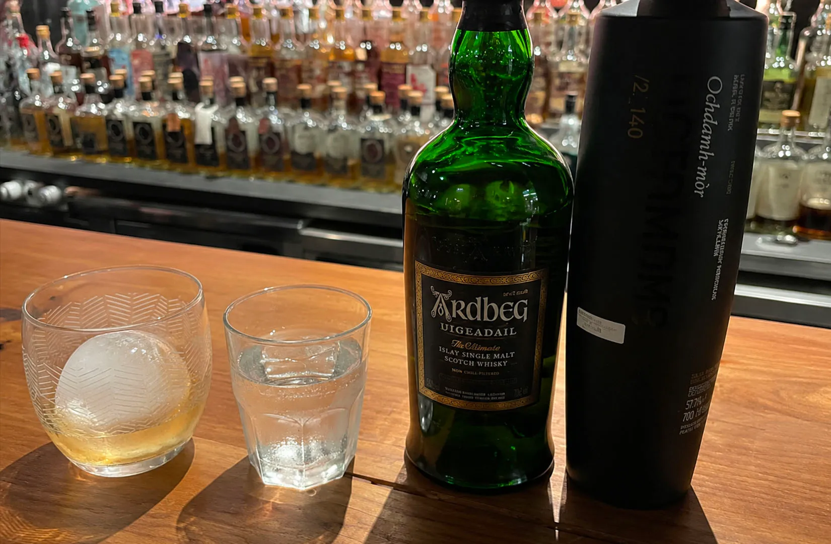 Ardbeg whisky bottle with two glasses on a bar counter.