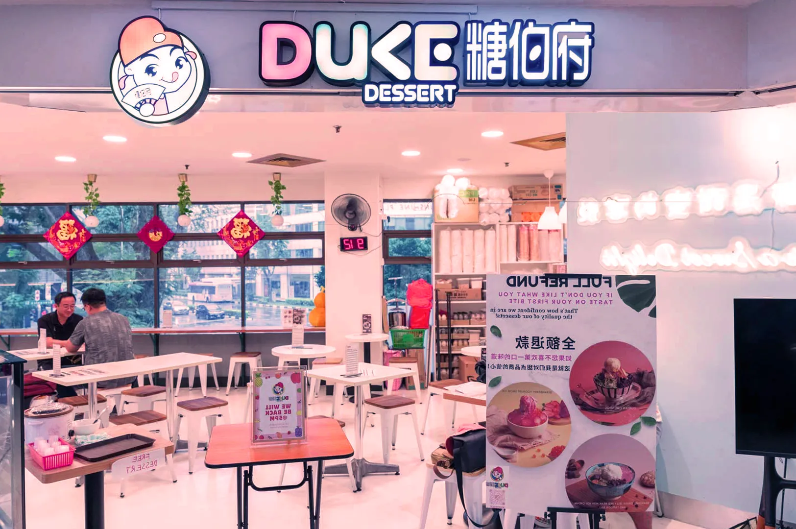 Brightly lit dessert shop named "Duke Dessert," featuring colorful signage, festive red decorations, modern décor, and customers seated at tables.