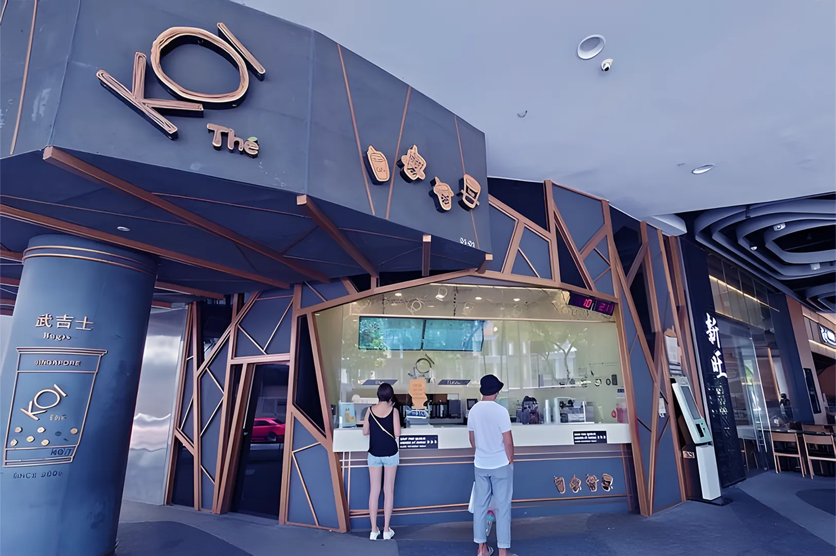 Modern bubble tea shop with angular design, dark tones, and copper accents. Two people stand at the counter, creating a lively, urban atmosphere.
