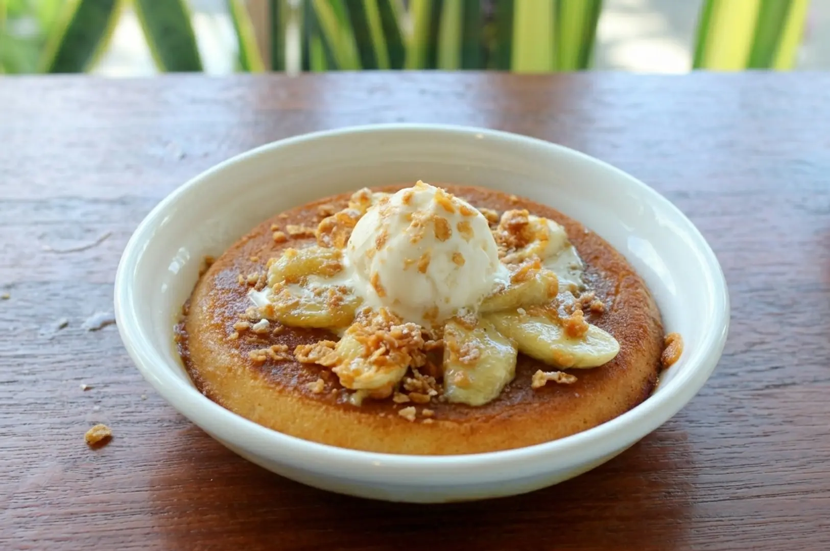 Soufflé pancake with banana slices, vanilla ice cream, and crushed nuts on wooden table