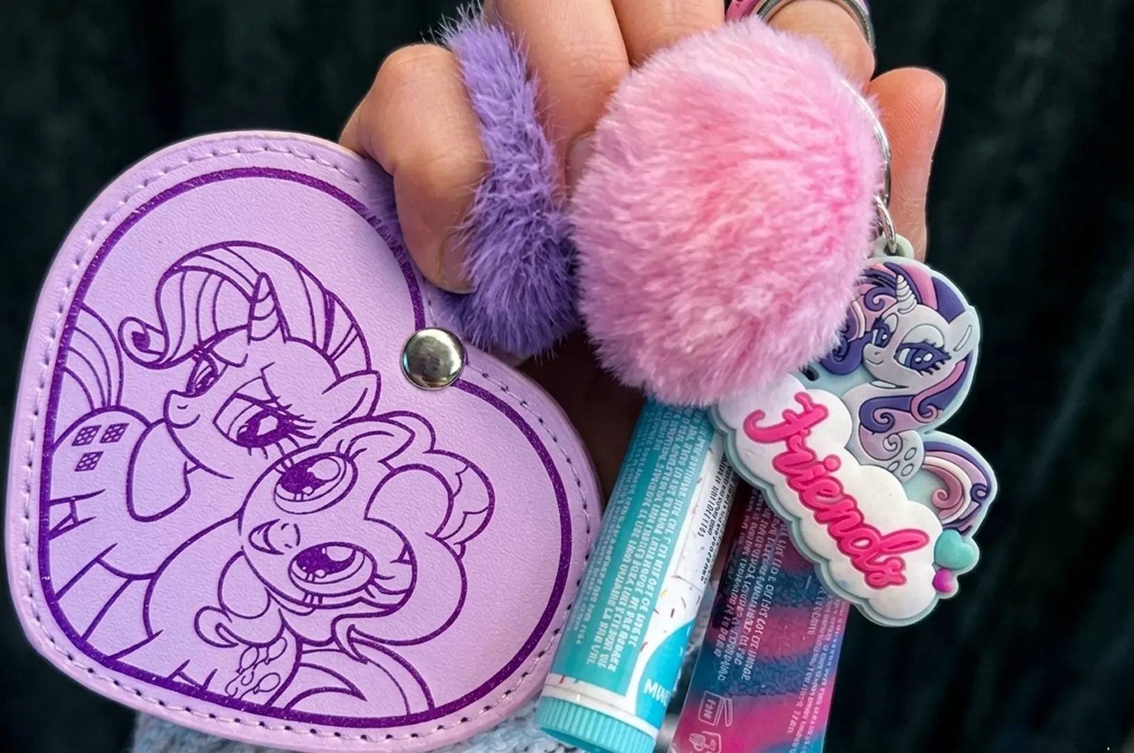 Purple heart-shaped My Little Pony Rarity pouch with fuzzy pom-pom keychains and lip balms.