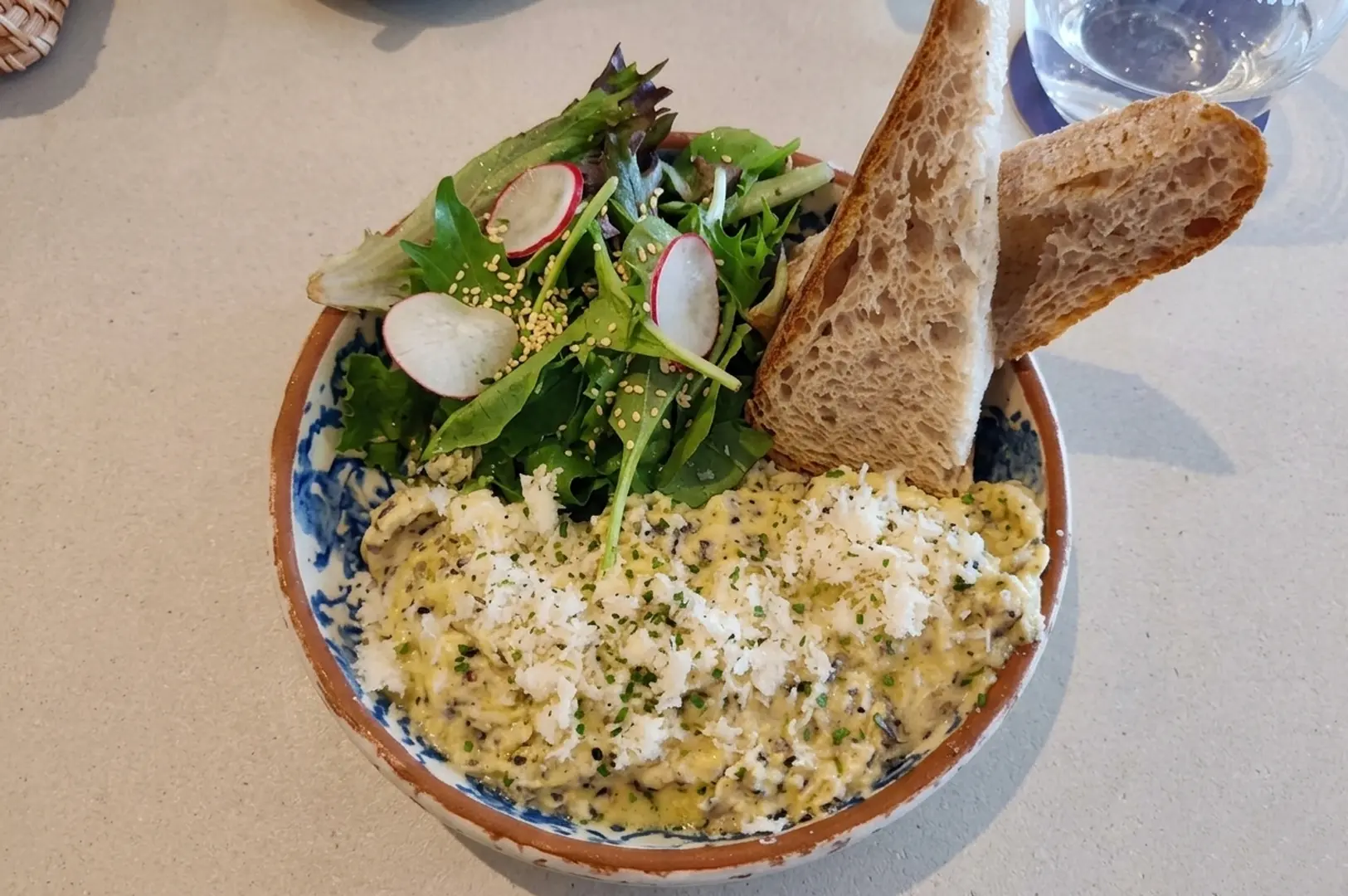 Truffle scrambled eggs with grated cheese, fresh salad with radishes, and sourdough toast in ceramic bowl
