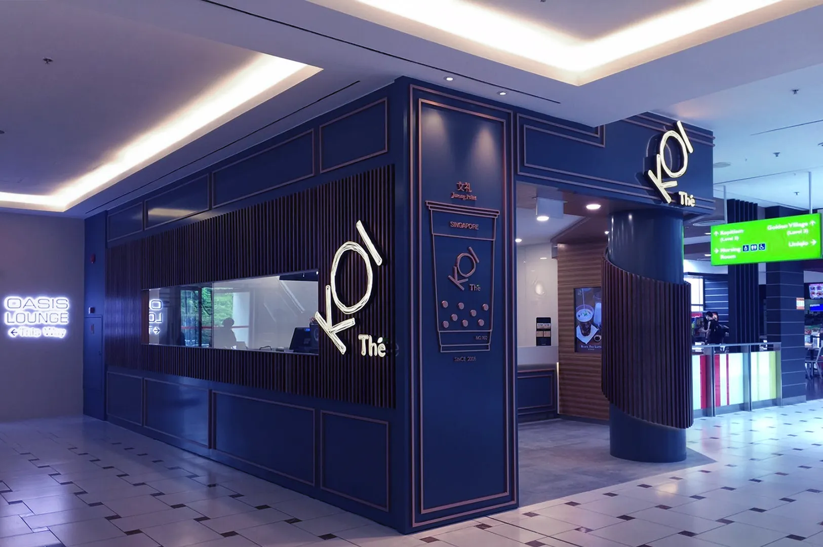 Modern bubble tea shop with dark blue and gold accents, featuring a large "KOI Thé" sign. Bright, inviting ambiance with sleek interior design.