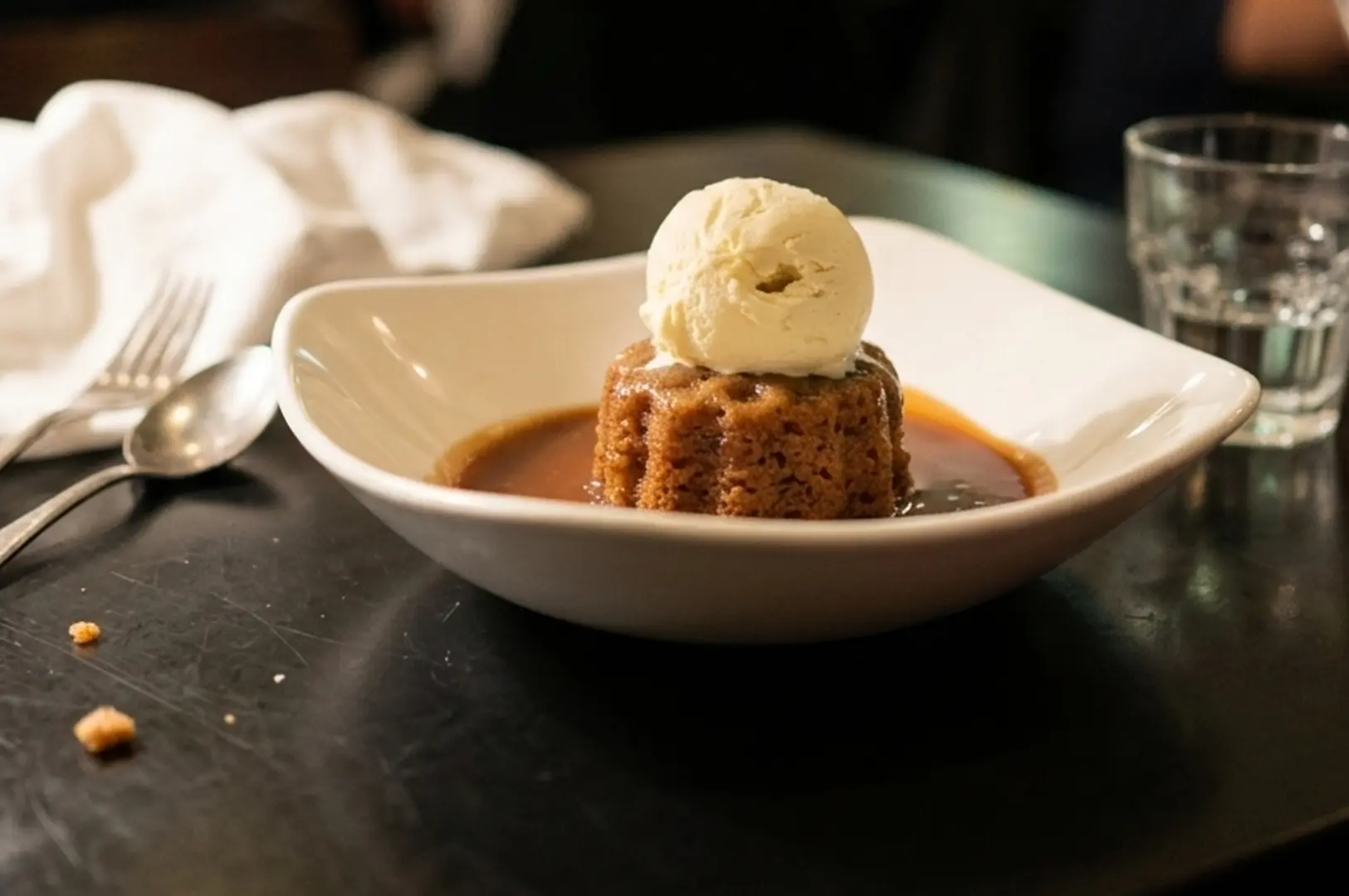 Sticky date pudding topped with vanilla ice cream and caramel sauce in white bowl