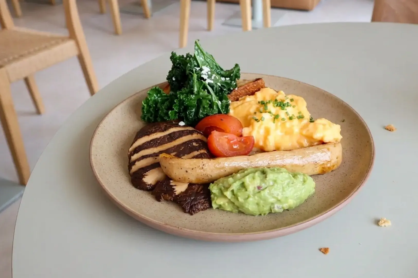Breakfast plate with scrambled eggs, grilled meat, sausage, tomatoes, kale, and guacamole on beige plate