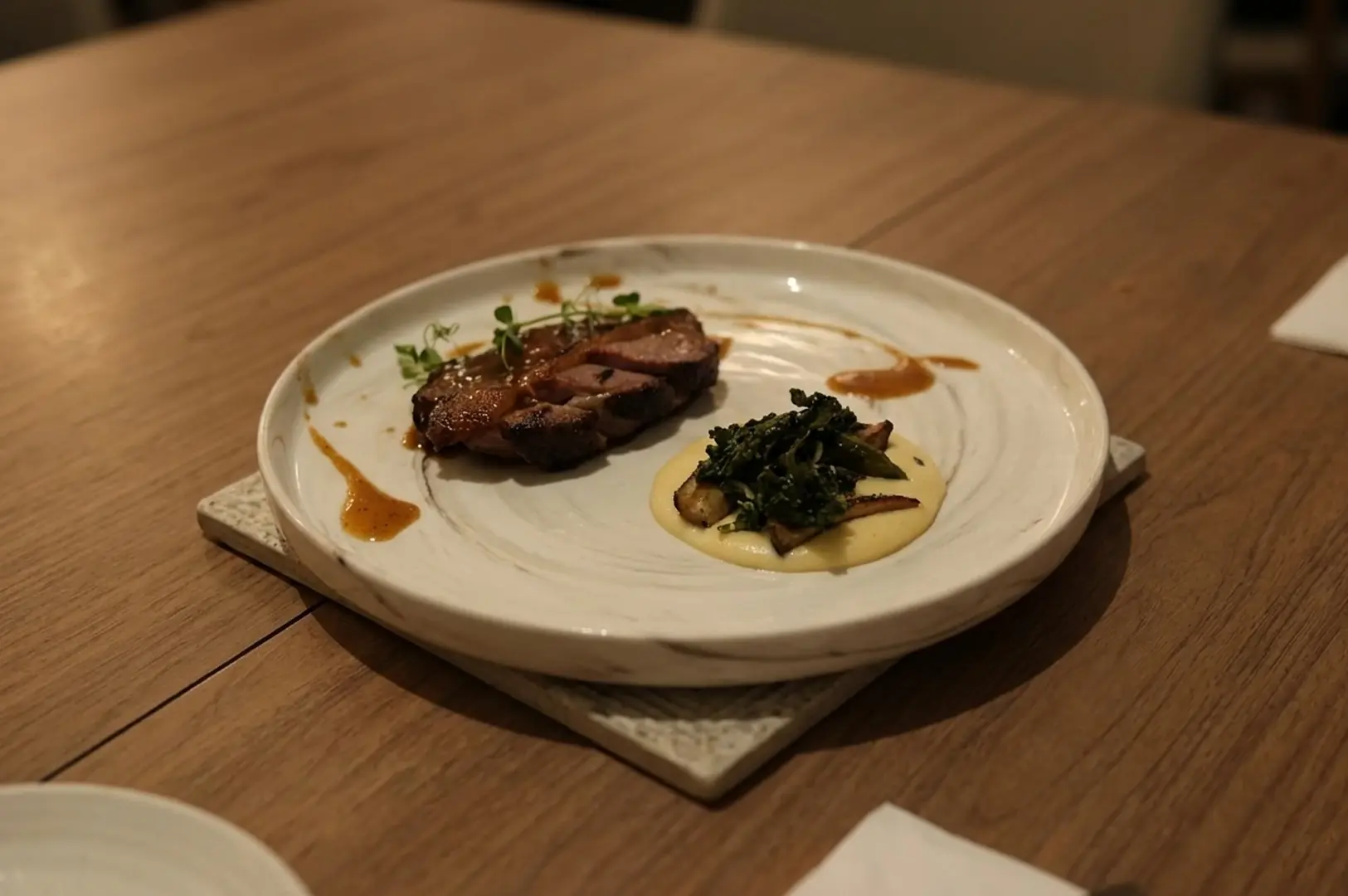 Sliced meat with sauce, creamy puree, and greens on a white plate