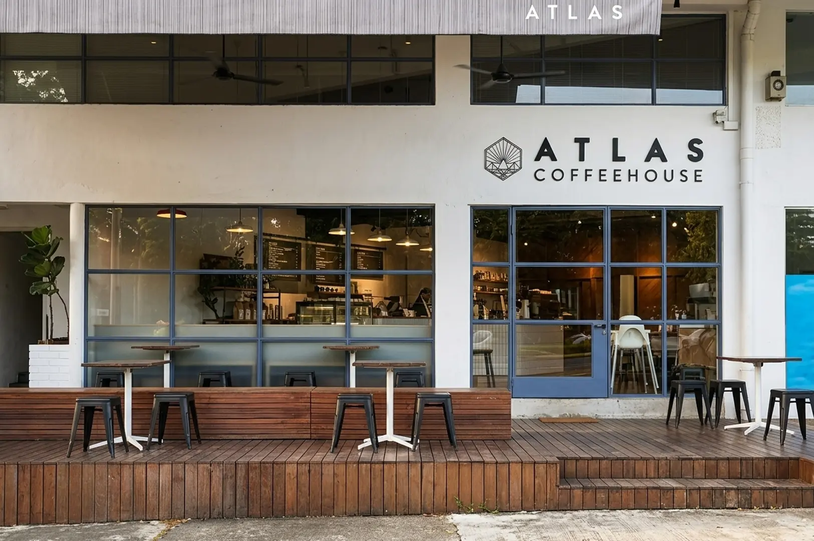 Exterior view of Atlas Coffeehouse showing a white facade with blue-framed windows and a wooden deck patio with tables and stools