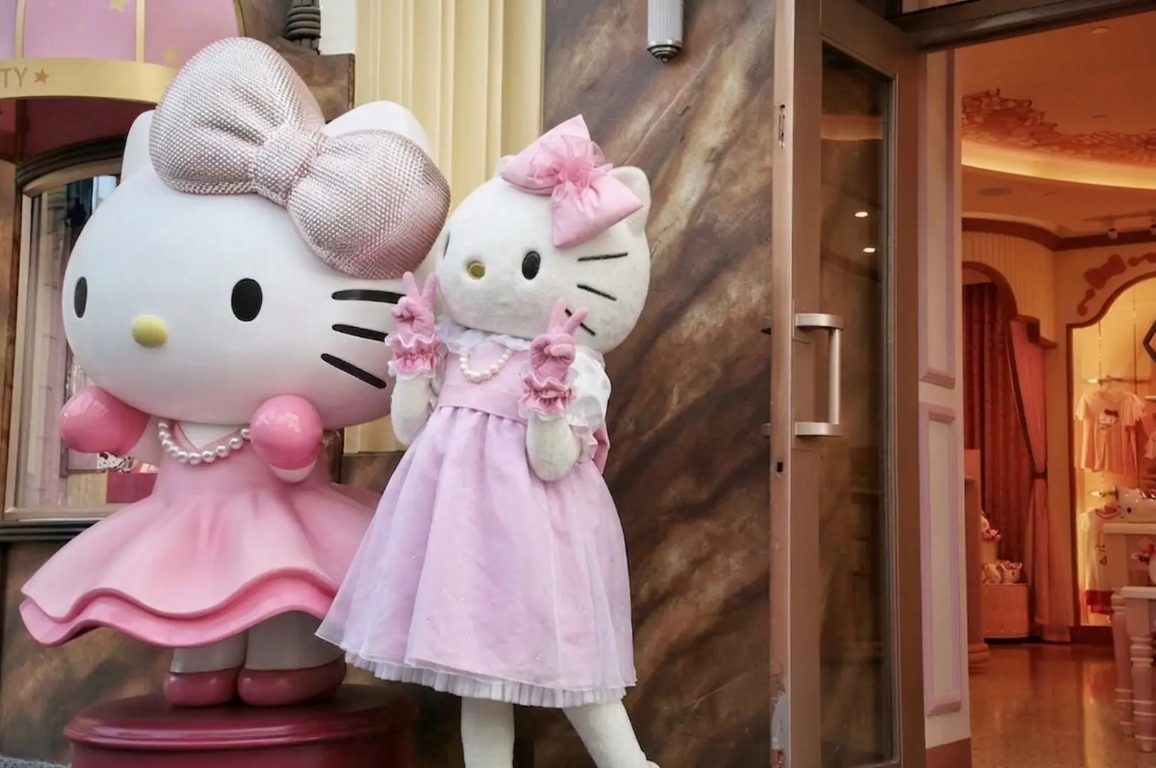 Two large Hello Kitty one statue and mascot in pink dresses at Superstar Boutique entrance, one with sparkly bow and another making peace signs