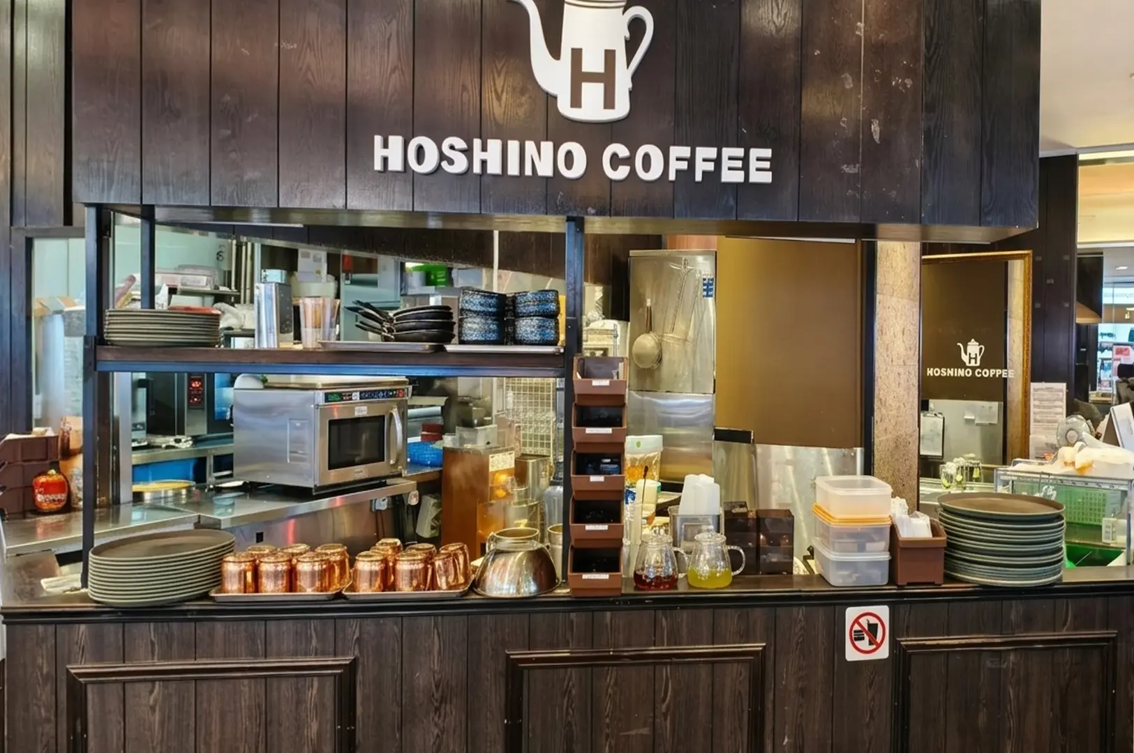 Hoshino Coffee service counter with dark wood paneling, displaying copper mugs, stacked plates, and kitchen equipment behind the glass