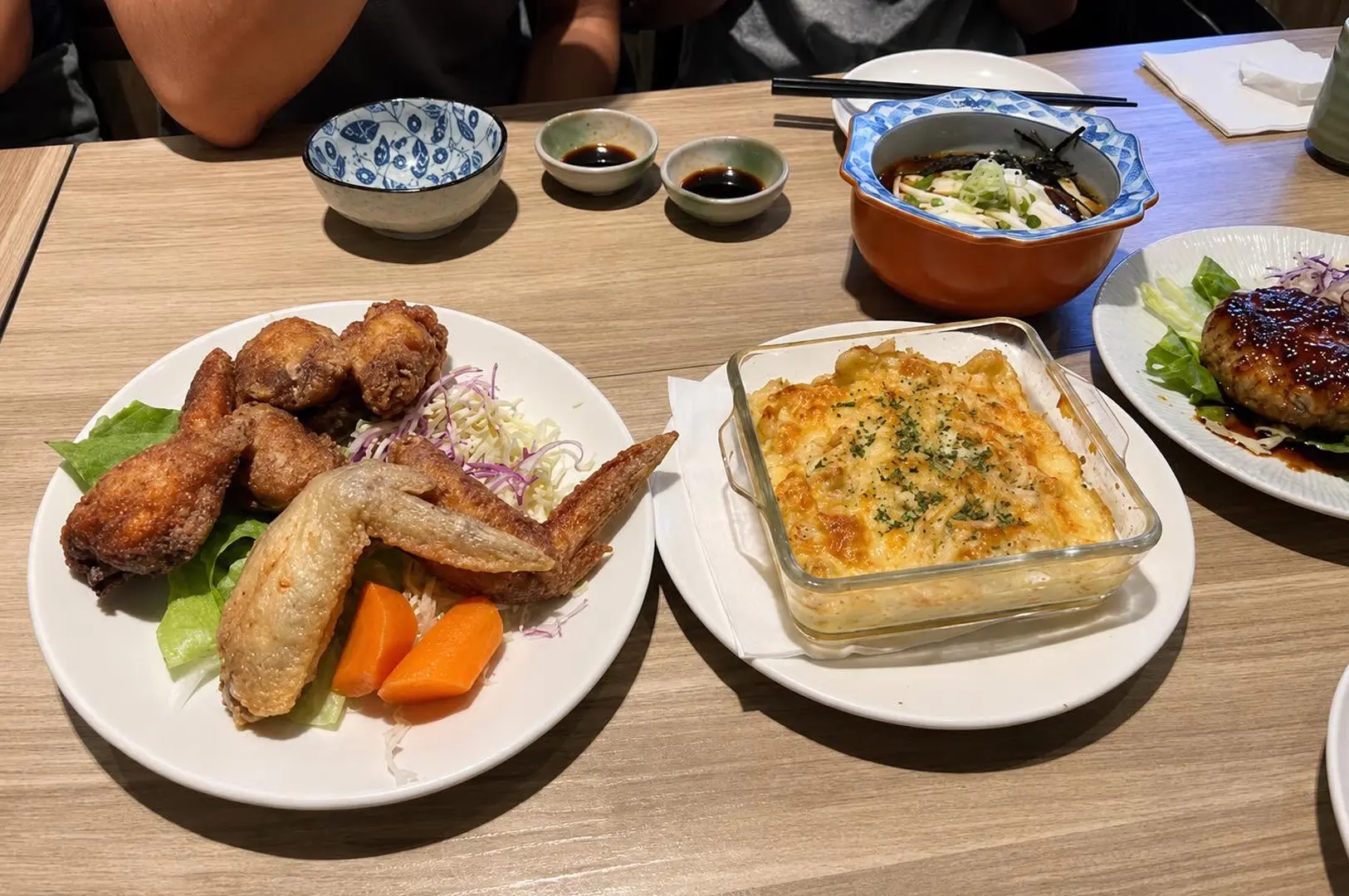 Japanese comfort food spread with fried chicken, baked gratin, hamburger steak, and noodle soup served on a dining table.