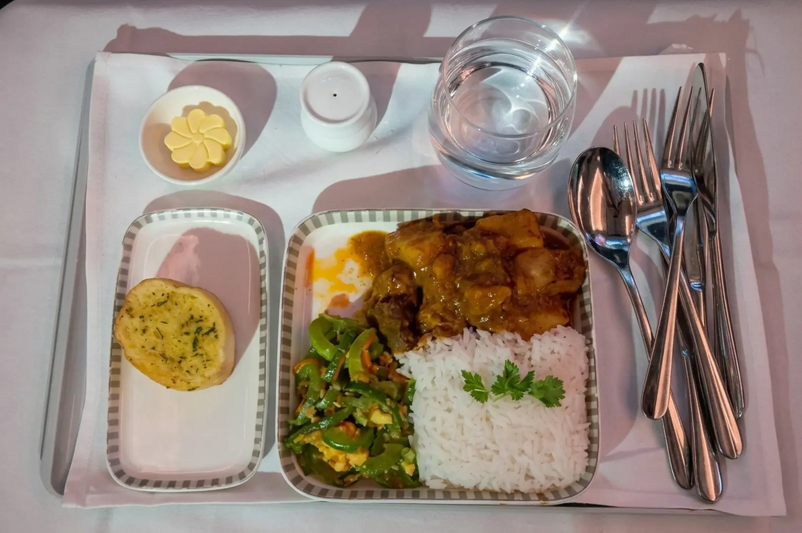 Airplane meal tray with rice, curry, vegetables, garlic bread and water