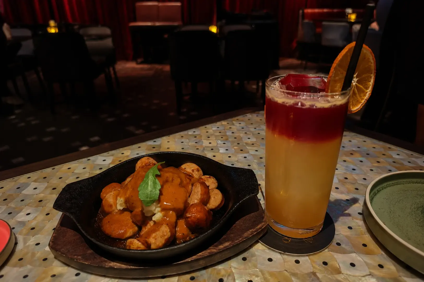 Layered cocktail with orange garnish and gnocchi dish on mother-of-pearl inlaid table at Quaich Bar