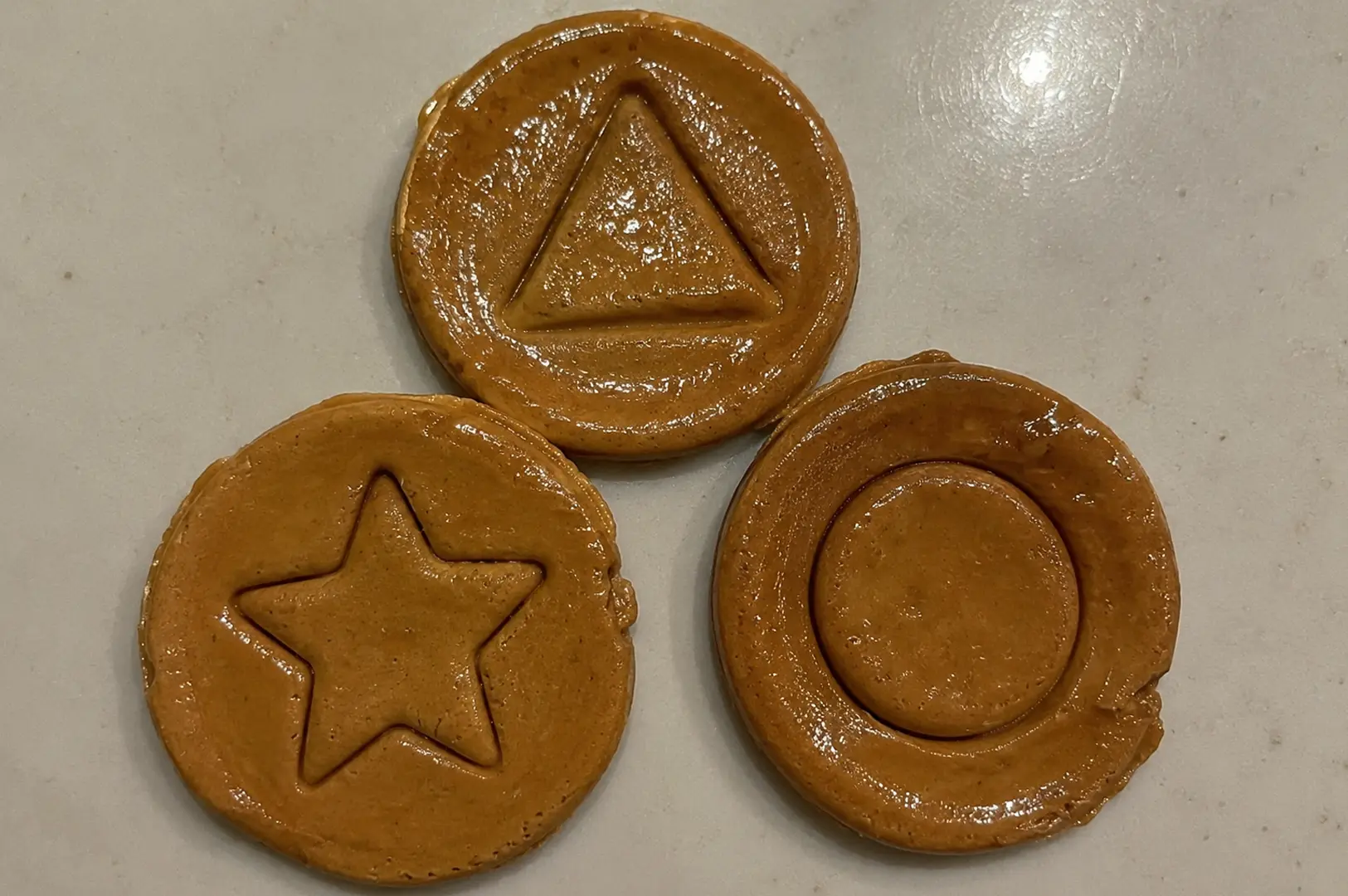 Three round Dalgona honeycomb candies featuring stamped triangle, star, and circle shapes
