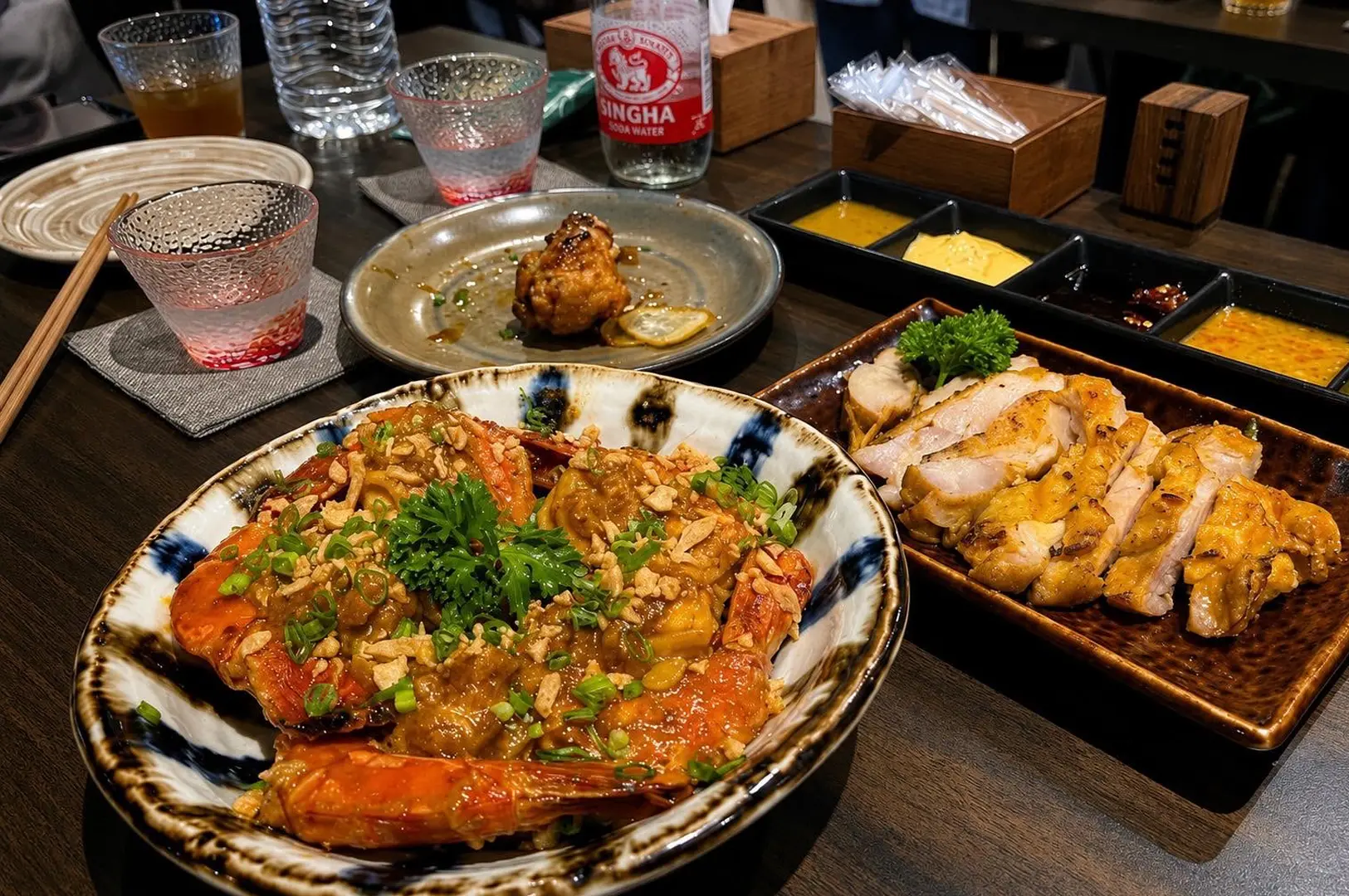 Large grilled prawns and sliced grilled chicken served with dipping sauces in a cozy Japanese restaurant.