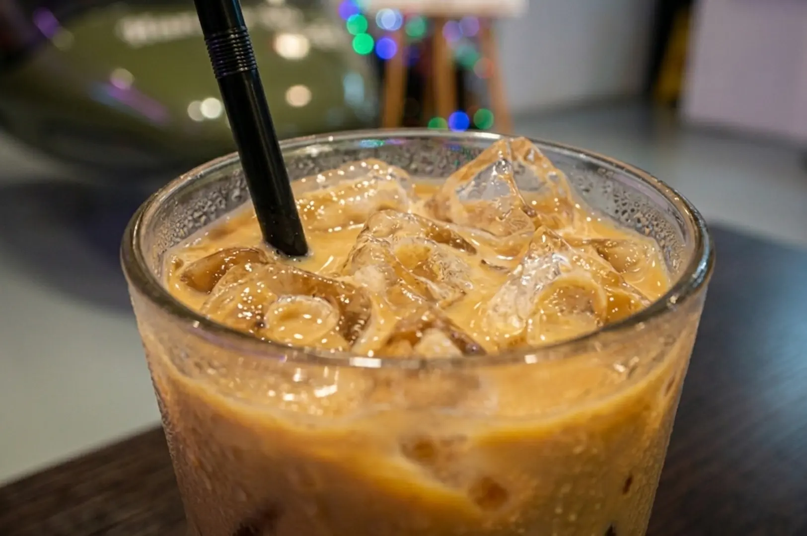 Iced coffee in a glass with a black straw on a table with blurred lights