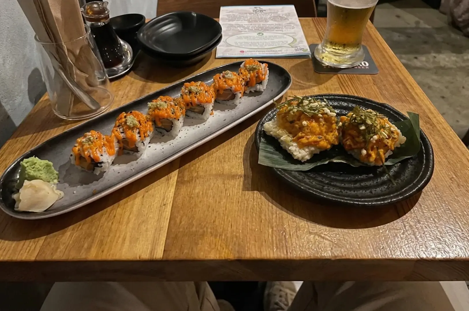 Sushi platter with spicy rolls and nigiri served on a wooden table next to a glass of beer