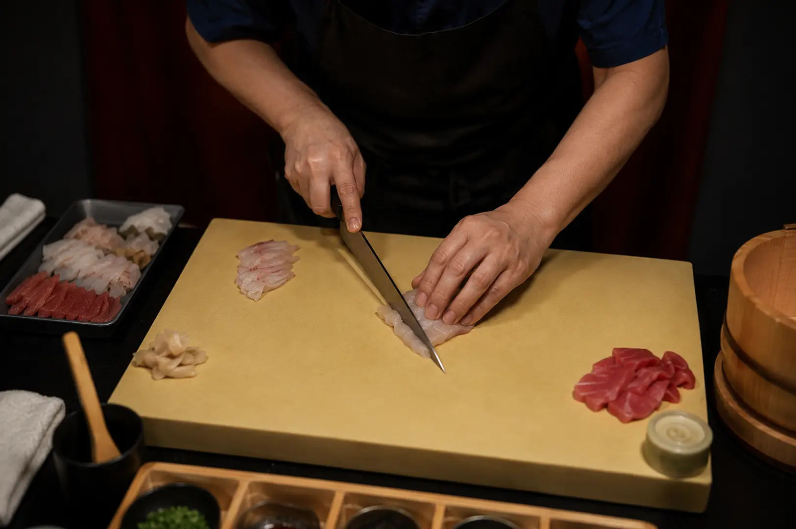 Sushi chef slicing fresh fish on a yellow cutting board with various sashimi cuts prepared nearby