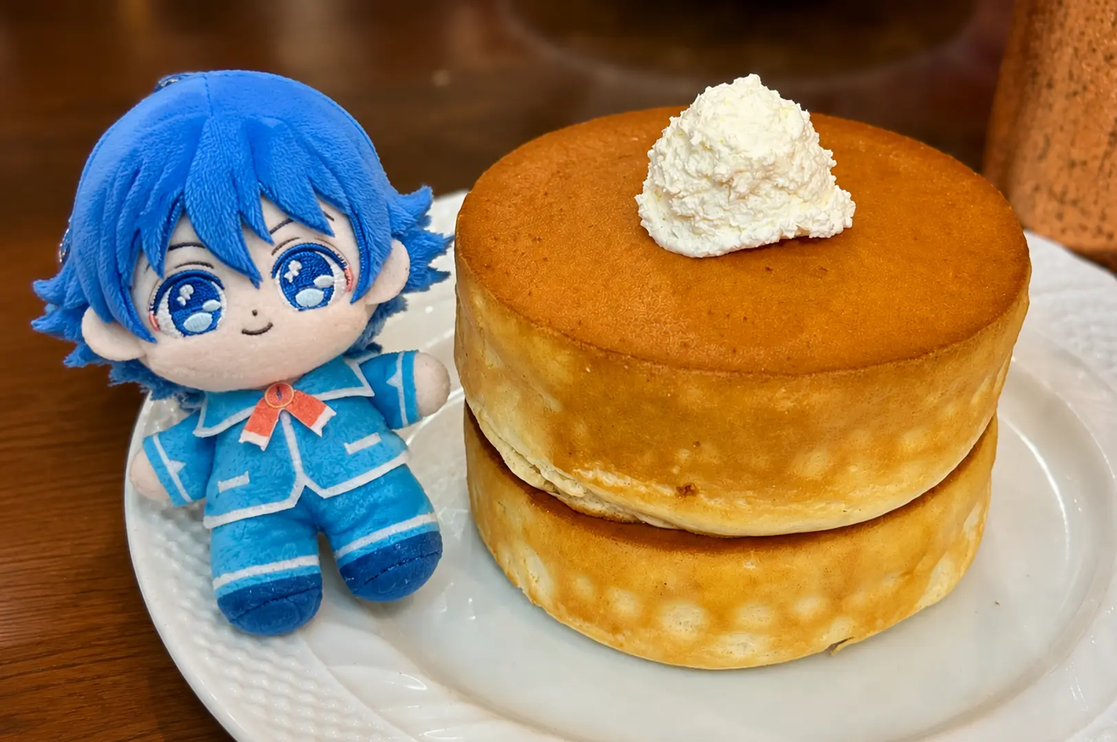 Stack of two fluffy souffle pancakes topped with whipped cream on a white plate next to a blue plush toy