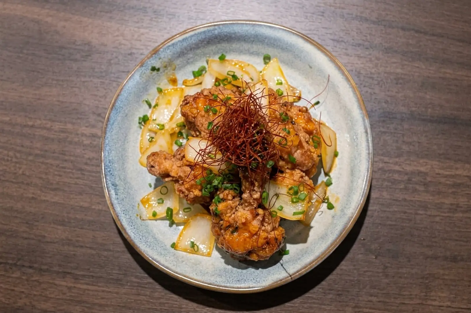 Japanese-Vietnamese fusion dish featuring crispy fried chicken with sliced vegetables, scallions, and crispy garnish on blue ceramic plate