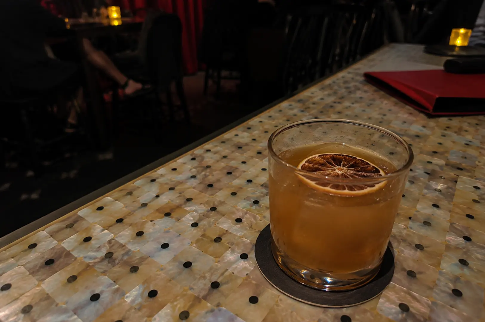 Whisky cocktail with dried citrus wheel on decorative mother-of-pearl table at dimly lit ba