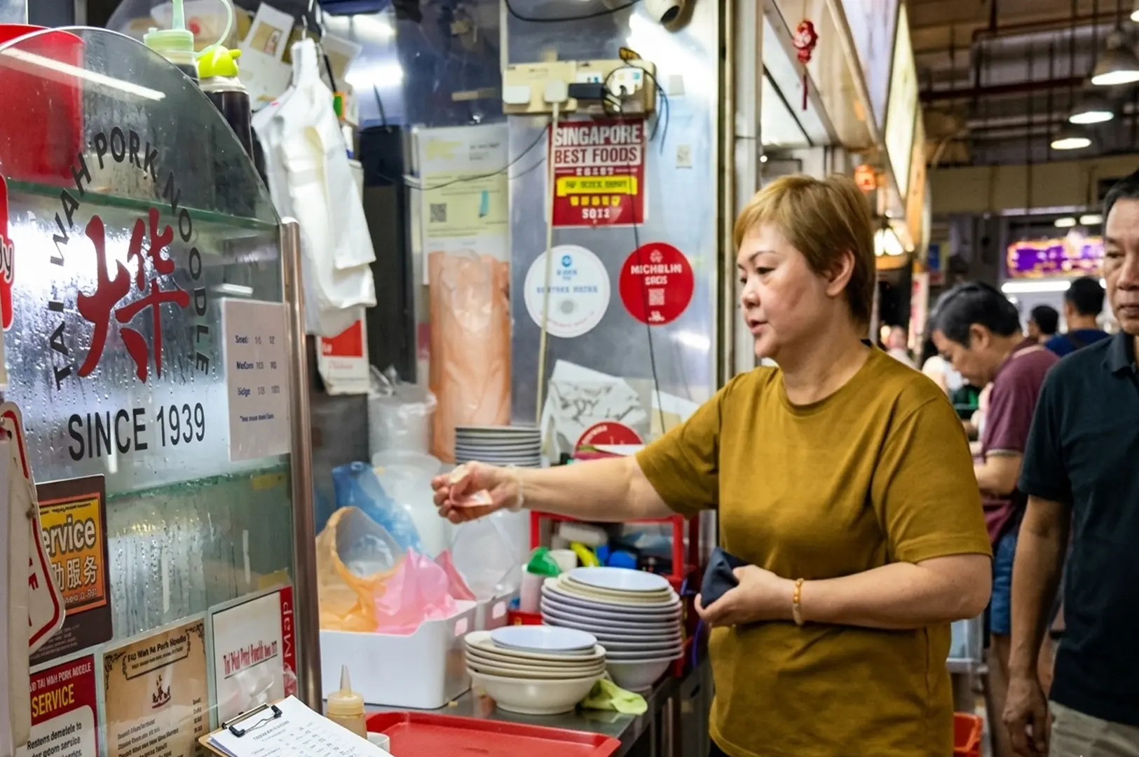 Woman ordering at Tai Wah Pork Noodle stall since 1939 with Michelin award visible