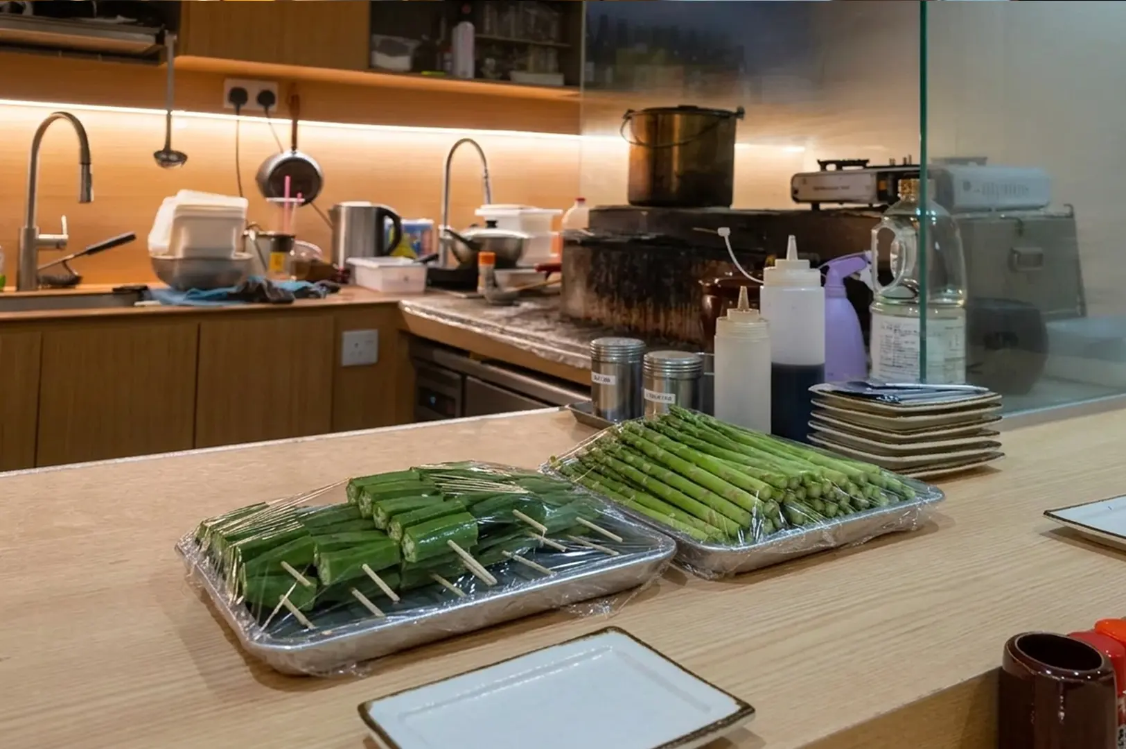 Trays of fresh okra skewers and asparagus prepped on the counter of TOYA's modern yakitori kitchen