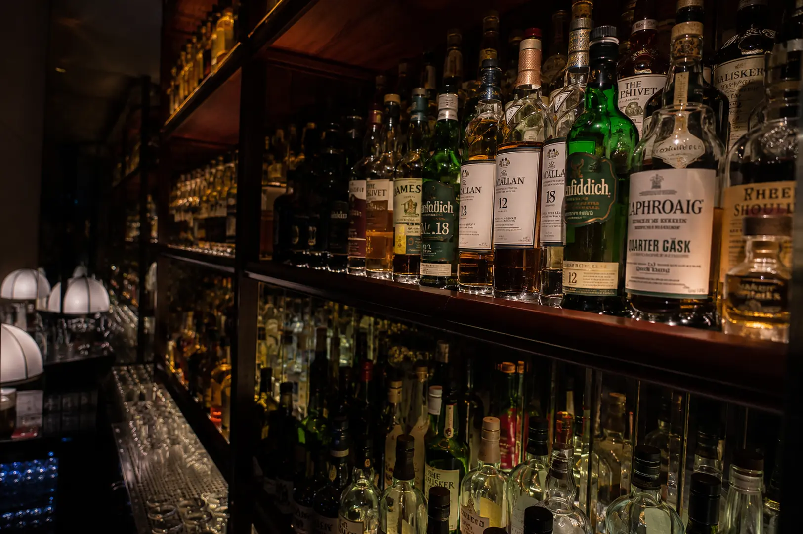Well-stocked shelves of premium whisky bottles including Glenfiddich and Laphroaig illuminated in the bar