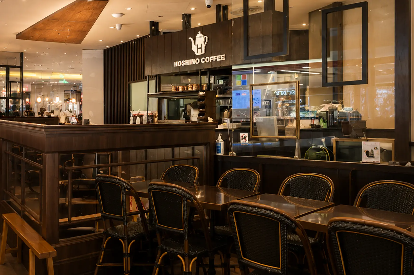 Interior of Hoshino Coffee featuring dark wooden furniture, wicker-backed bistro chairs, and the service counter with the illuminated logo