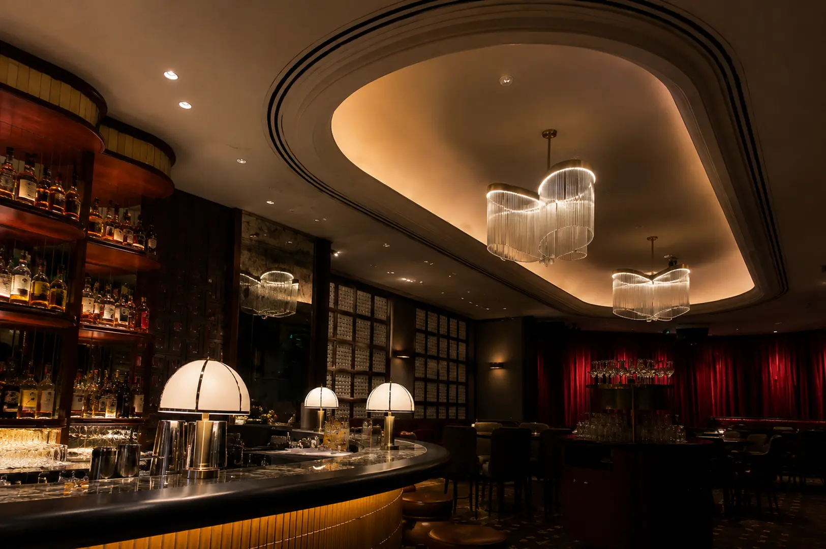 Elegant interior of Quaich Bar featuring curved bar, whisky shelves, modern chandeliers, and red velvet curtains