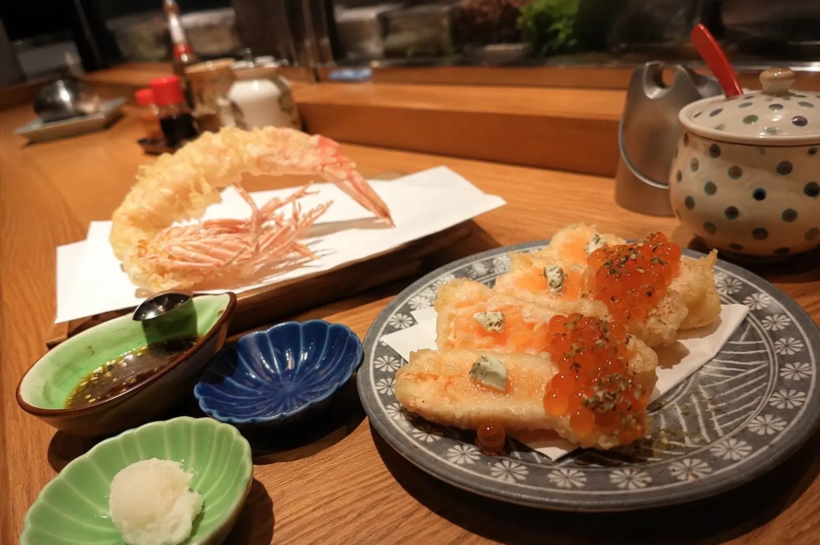 Crispy shrimp tempura and seafood topped with salmon roe served with dipping sauces on a wooden table.