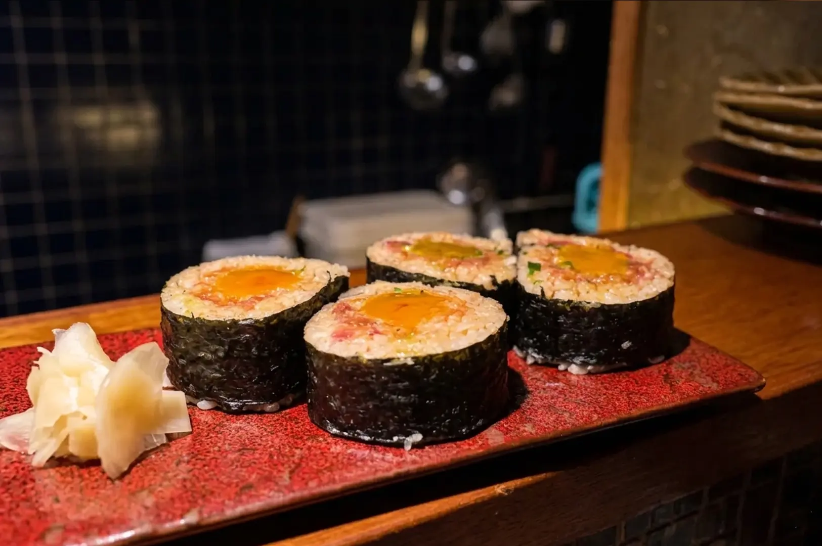 Thick futomaki sushi rolls topped with egg served on a red rectangular plate with pickled ginger at Apollon izakaya