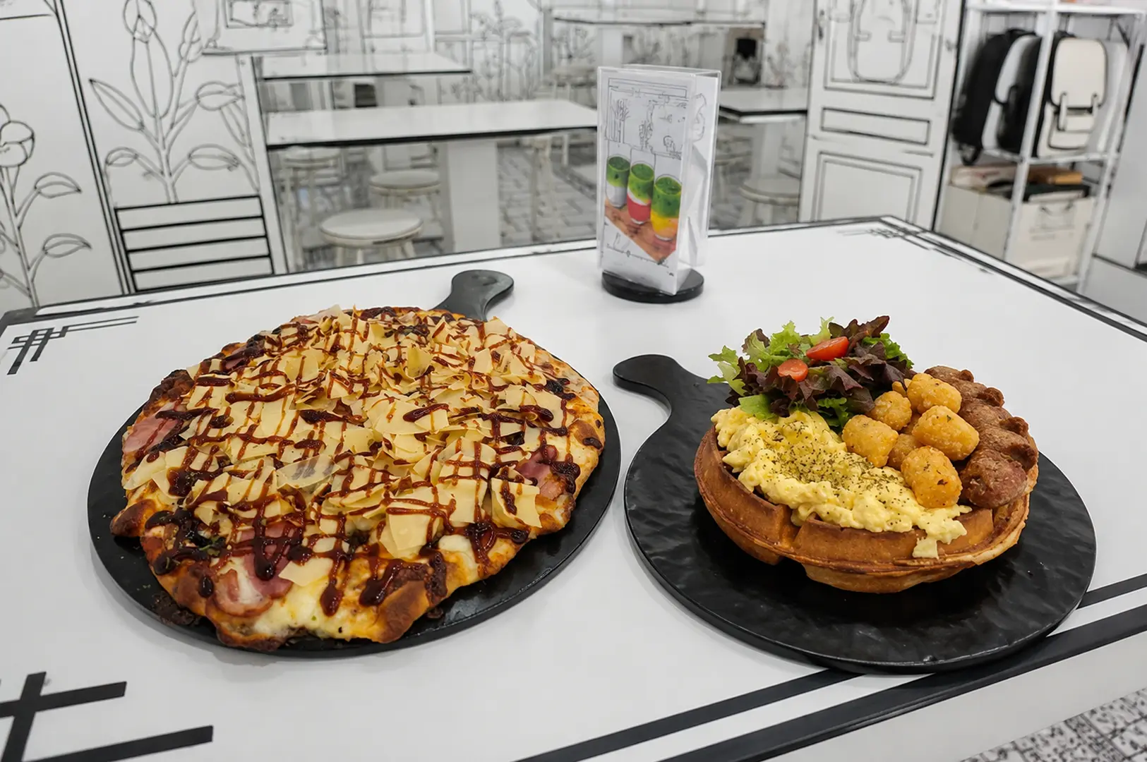 Pizza and savory waffle breakfast plates on black boards in a black-and-white illustrated cafe